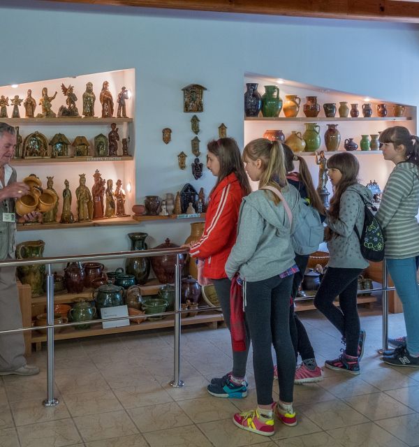 Grupa dziewczynek w wieku szkolnym zwiedza wystawę ośrodka tradycji garncarstwa w Chałupkach. Towarzyszy im przewodnik, który opowiada o jednym z eksponatów.
