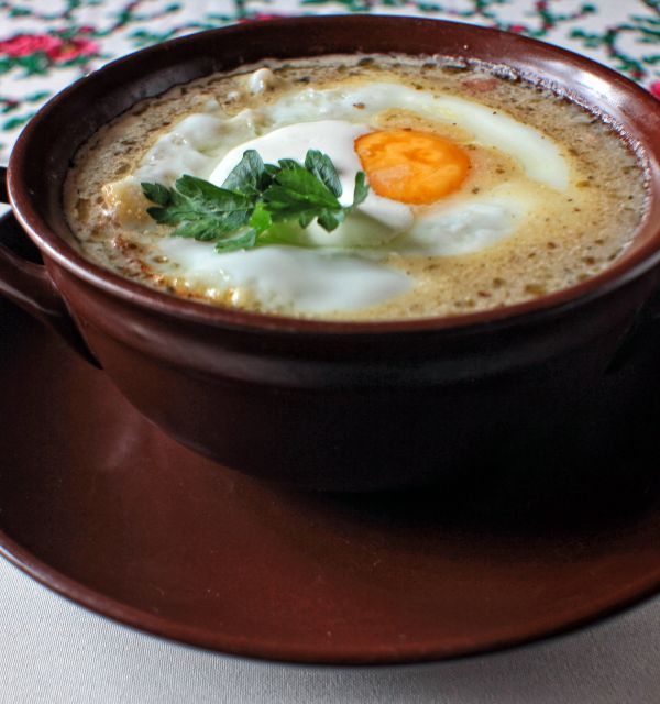 W ceramicznej misce zalewajka z jajkiem sadzonym. Danie udekorowane pietruszką.