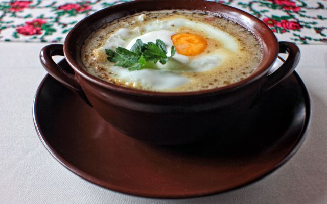 W ceramicznej misce zalewajka z jajkiem sadzonym. Danie udekorowane pietruszką.